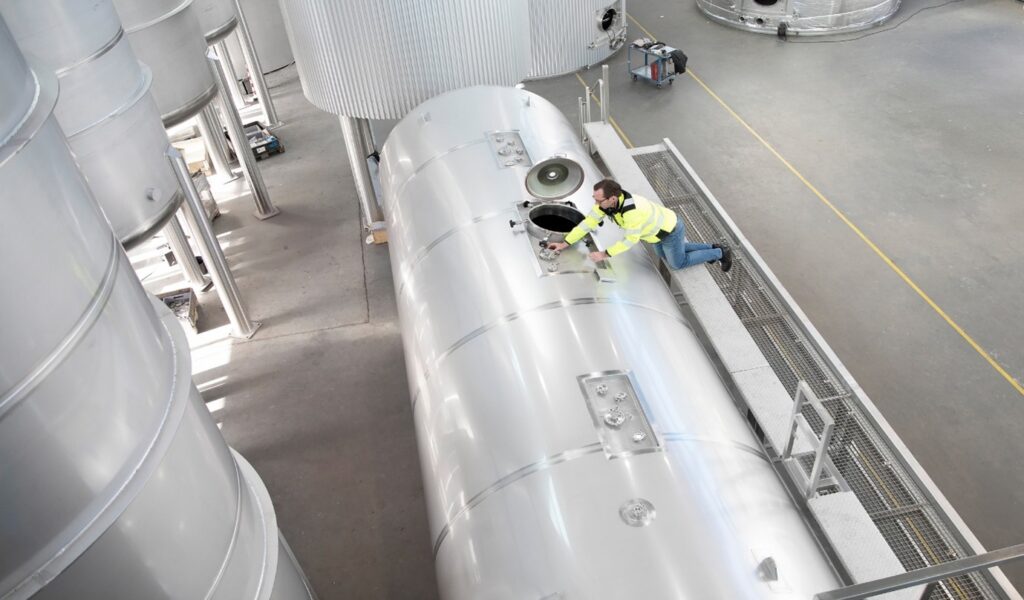 Technician standing on a platform inspecting a stainless steel tank from Gpi Pharma in a clean industrial environment.